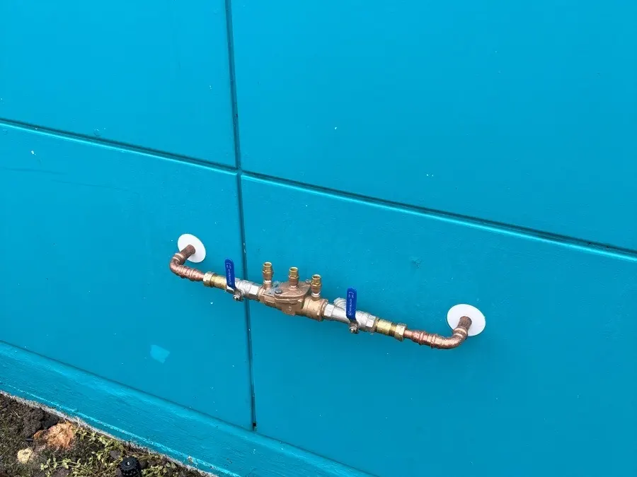 A double check backflow valve with blue isolating valves on a blue wall