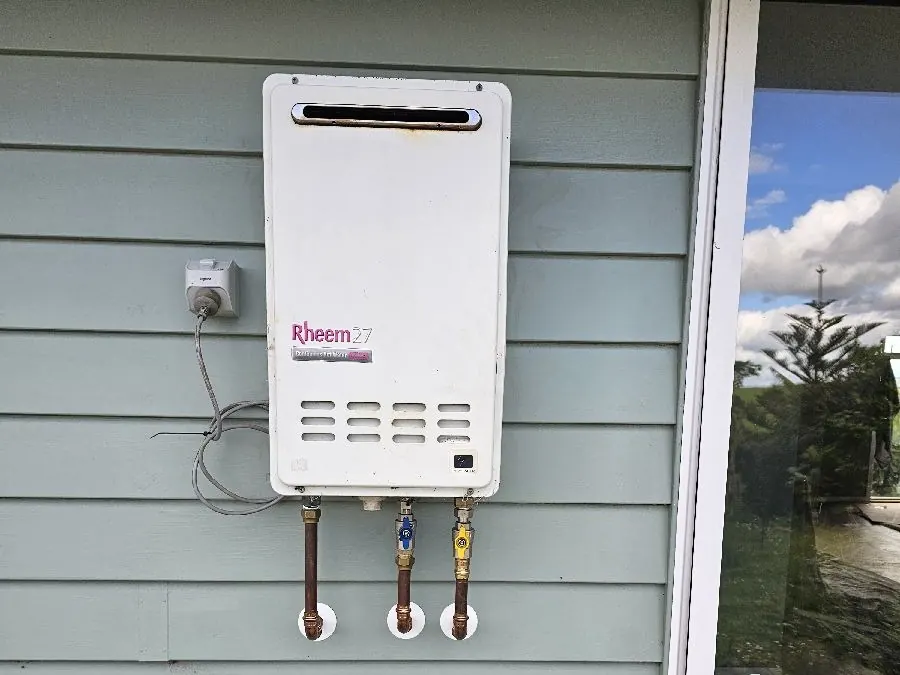A gas califont on a weatherboard wall, with its gas and water connections