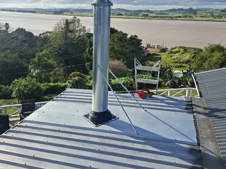 A new stainless steel flue with stays on a metal roof, looking over the river at Te Kōpuru
