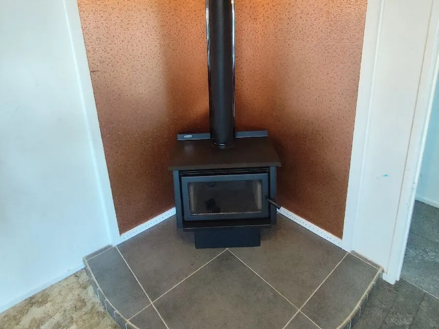 A new wood burner on a tiled corner hearth, where an old pot belly stove used to be
