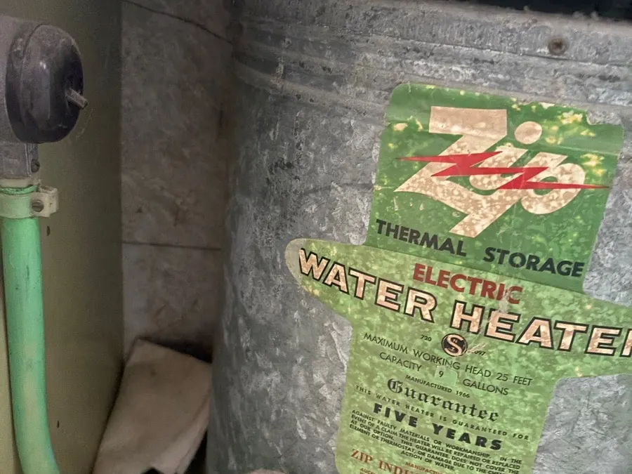 An old galvanised electric hot water cylinder with a faded label, before it was replaced