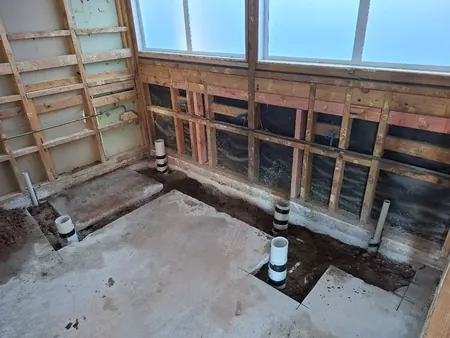 The concrete floor cut and new waste risers laid in a stripped-back toilet block